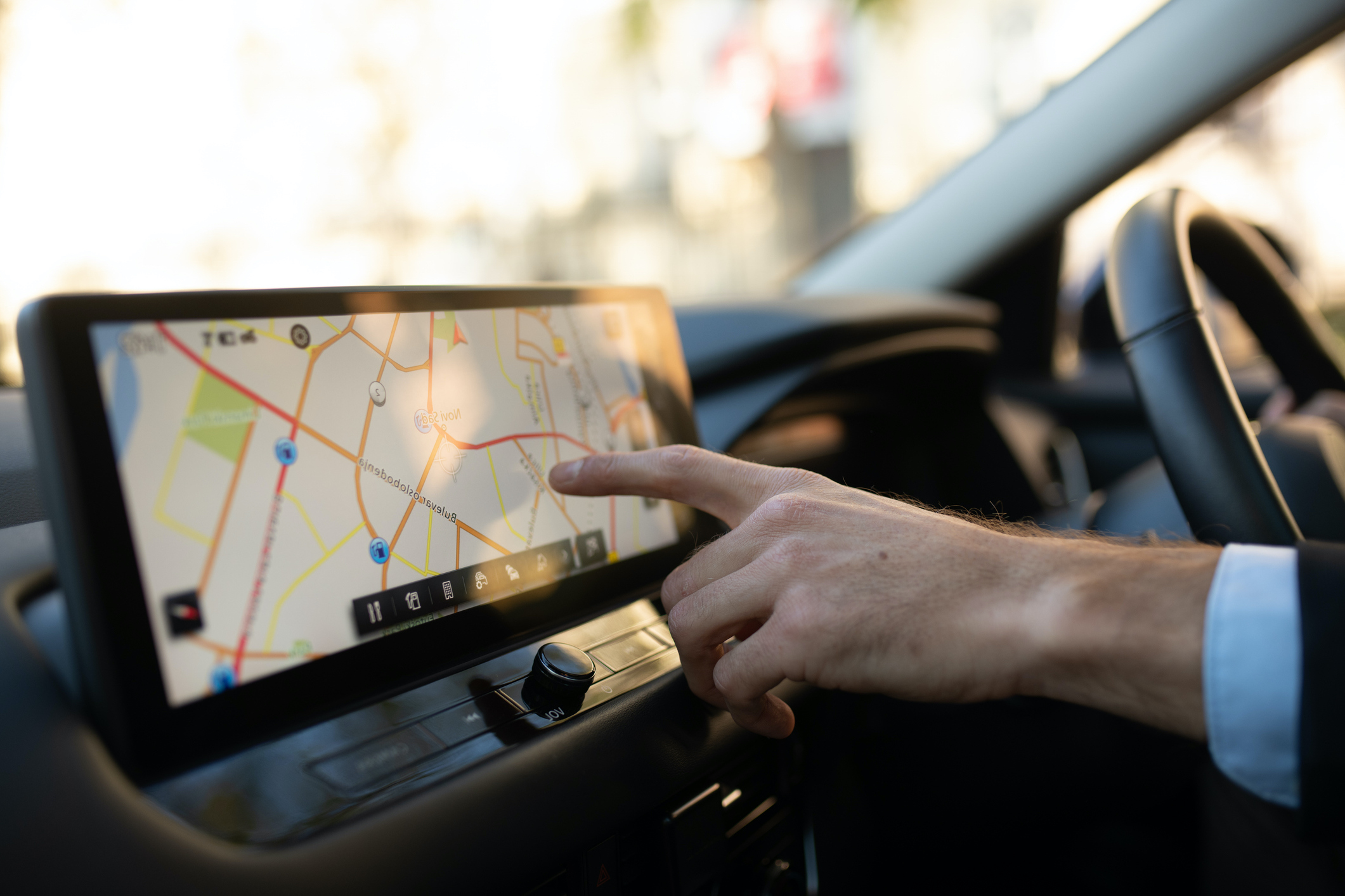 Close-up of a businessman’s hand adjusting the GPS on a modern car touchscreen. The man is sitting behind the wheel, wearing a suit, using the navigation system while driving, concept of business travel and technology.