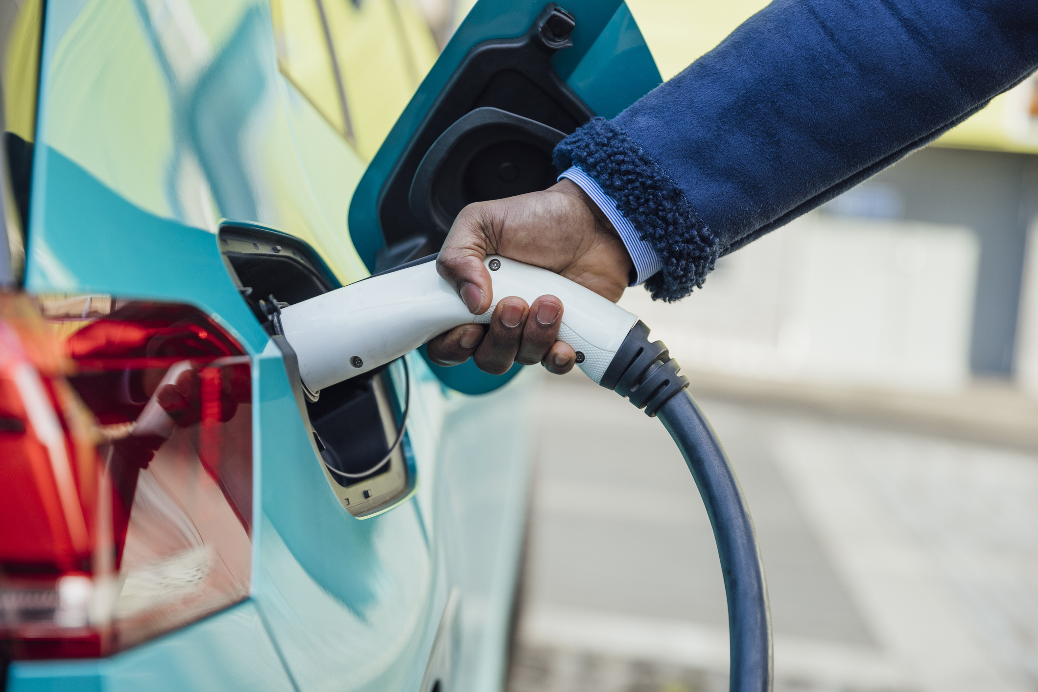 A side view close up shot of an unrecognisable mid adult businessman wearing formal business wear putting his electric car on charge at a public charging point in Newcastle upon Tyne in the North East of England.