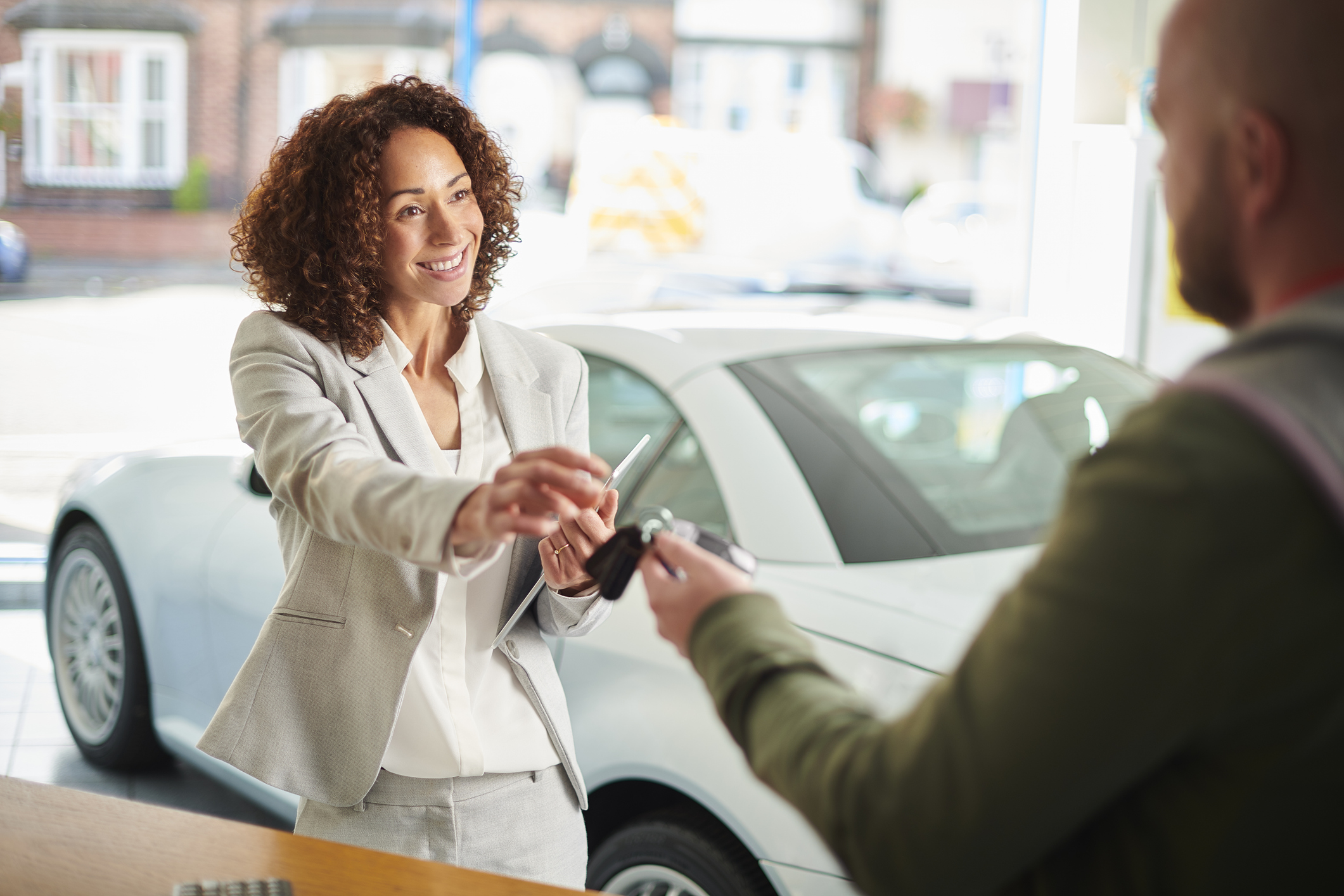 smiley car saleswomen handing over car keys to male customer