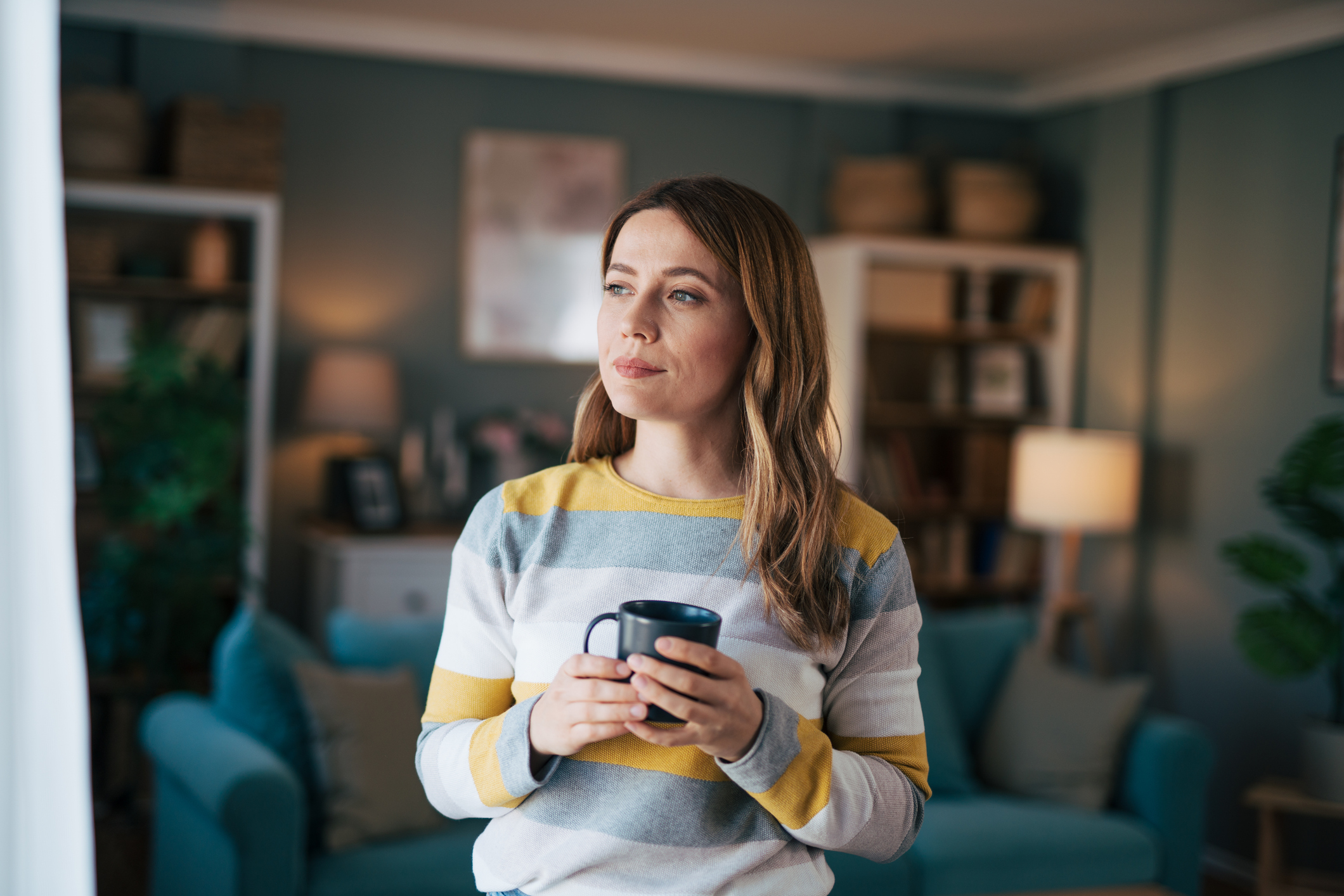 Mature woman looks out the window and drinks coffee.