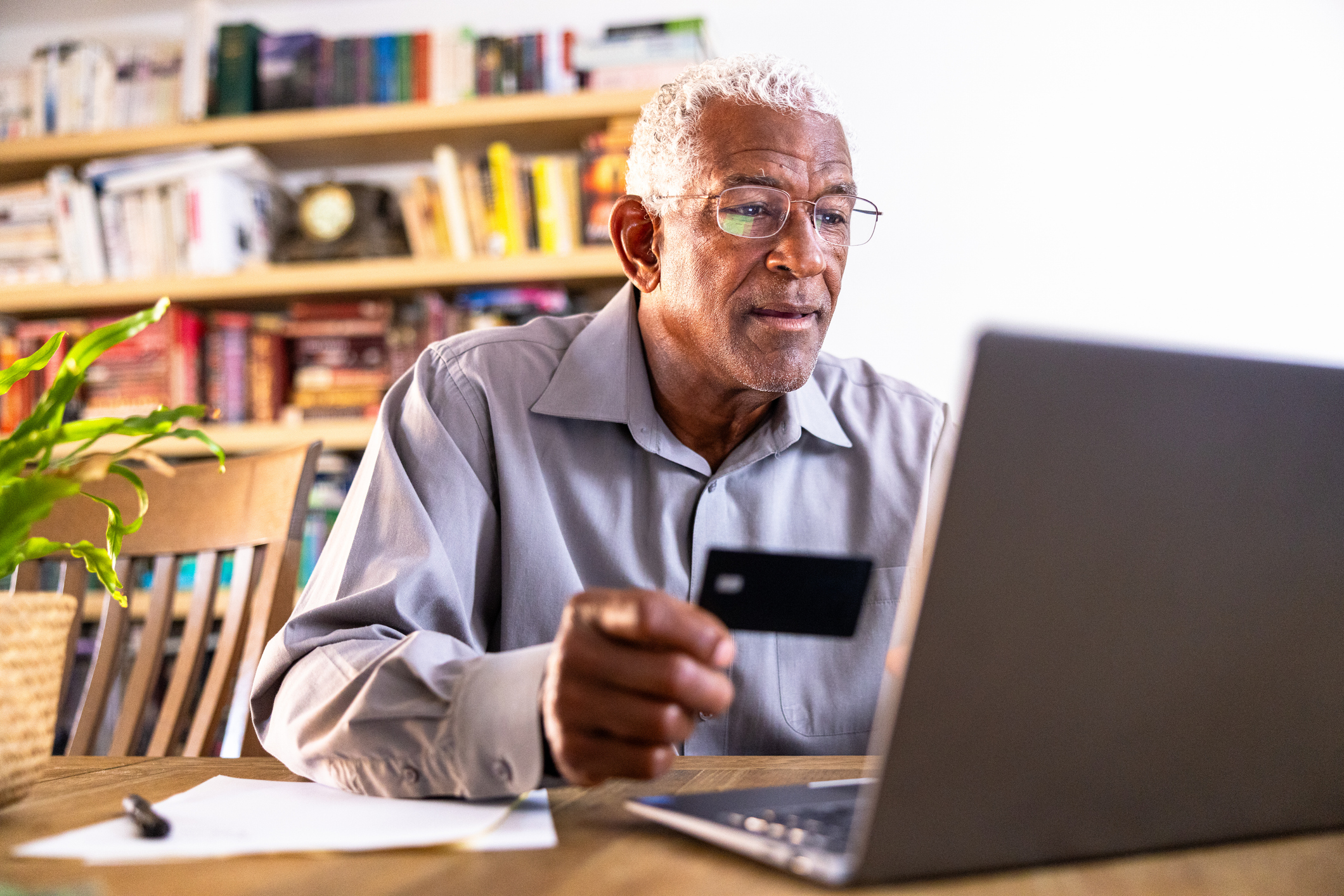 A senior black man shopping online using a credit card an a laptop.