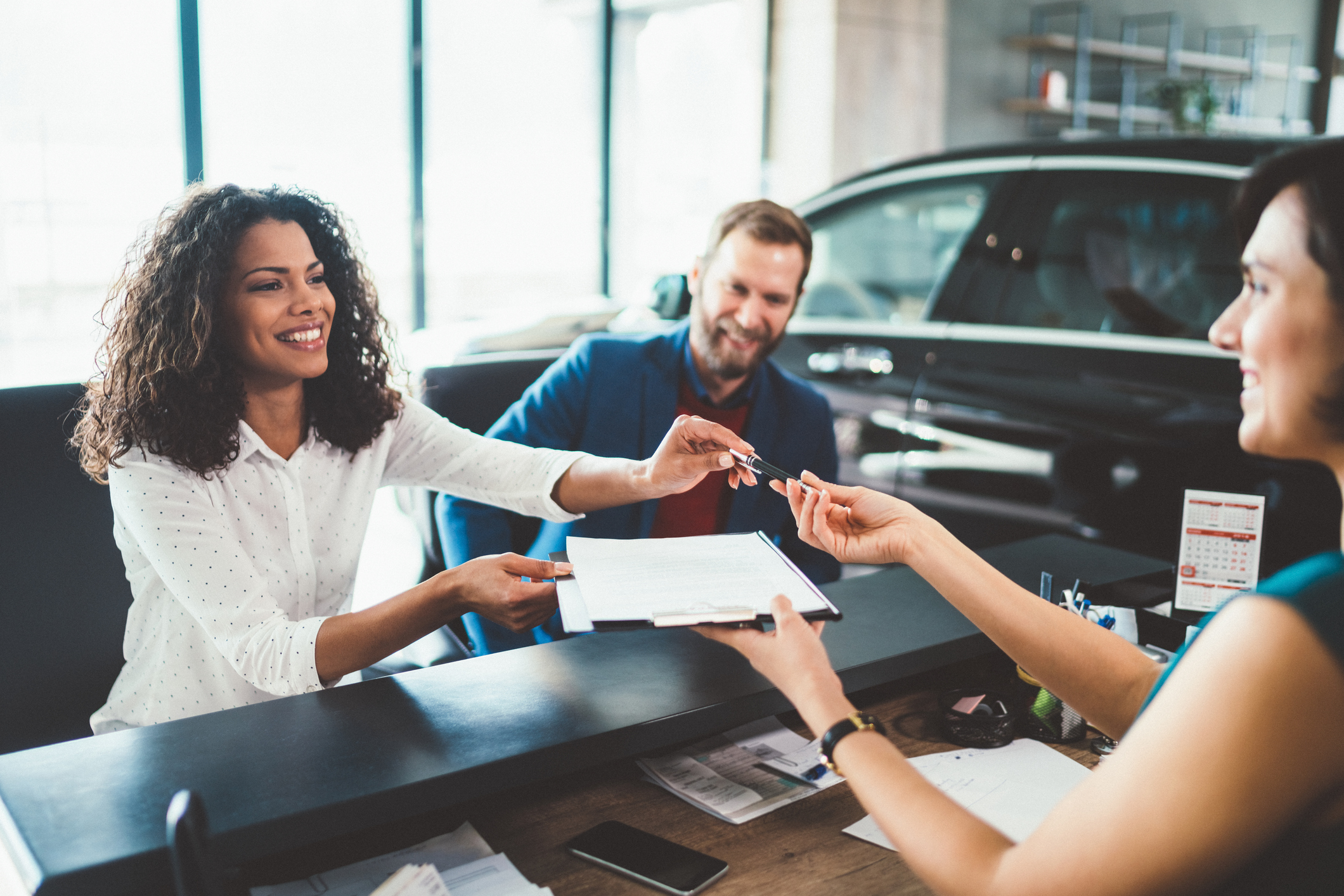 Young woman with her husband signing contract for buying a car.