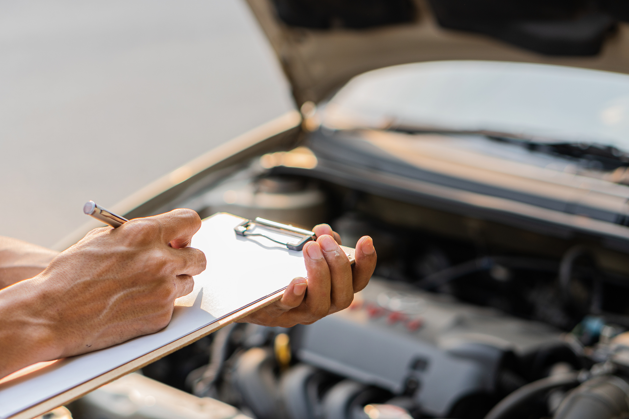 The auto mechanic checks the car engine with the check written in the car service engine repair checklist notebook.