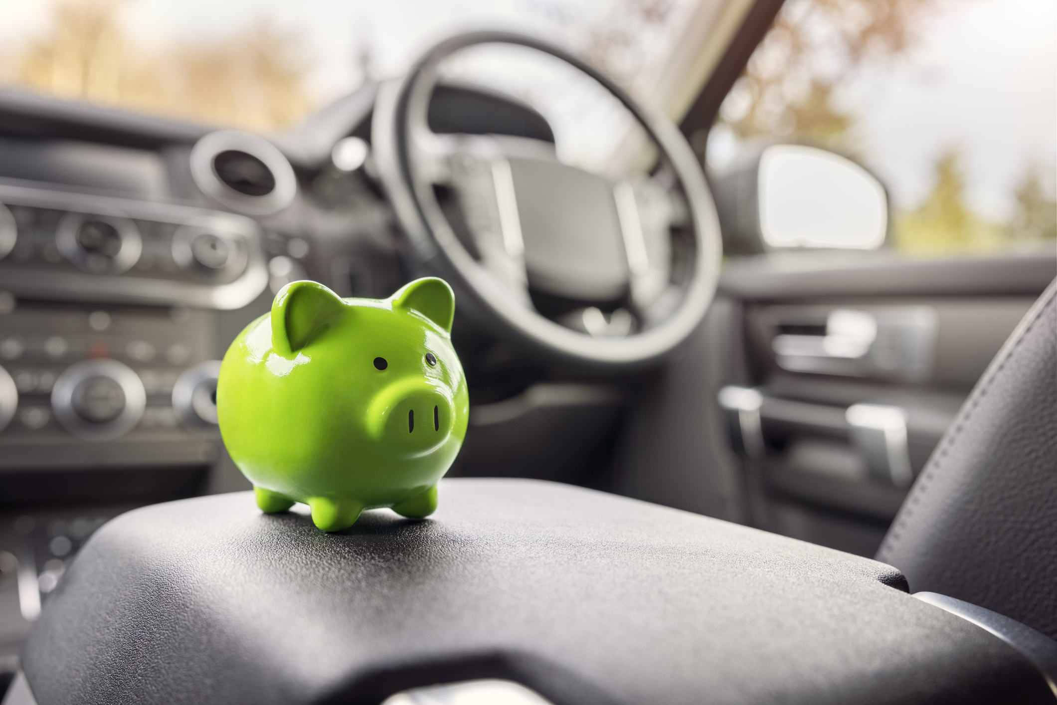 Green piggy bank money box in car interior, vehicle purchase, insurance or driving and motoring cost. 