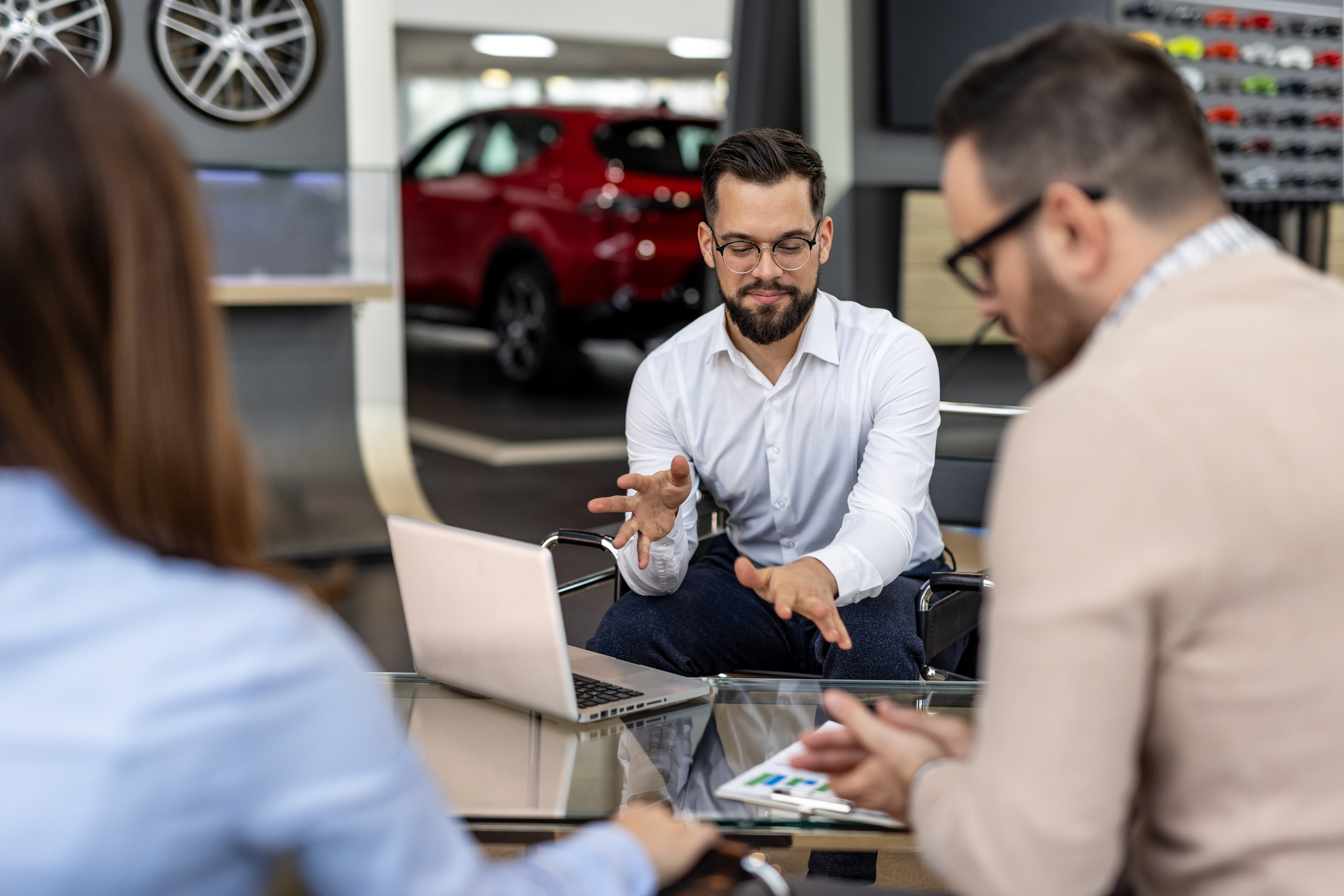 Car salesman explaining car features to a couple of customers using a laptop in a car dealership, they are discussing the purchase of a new vehicle