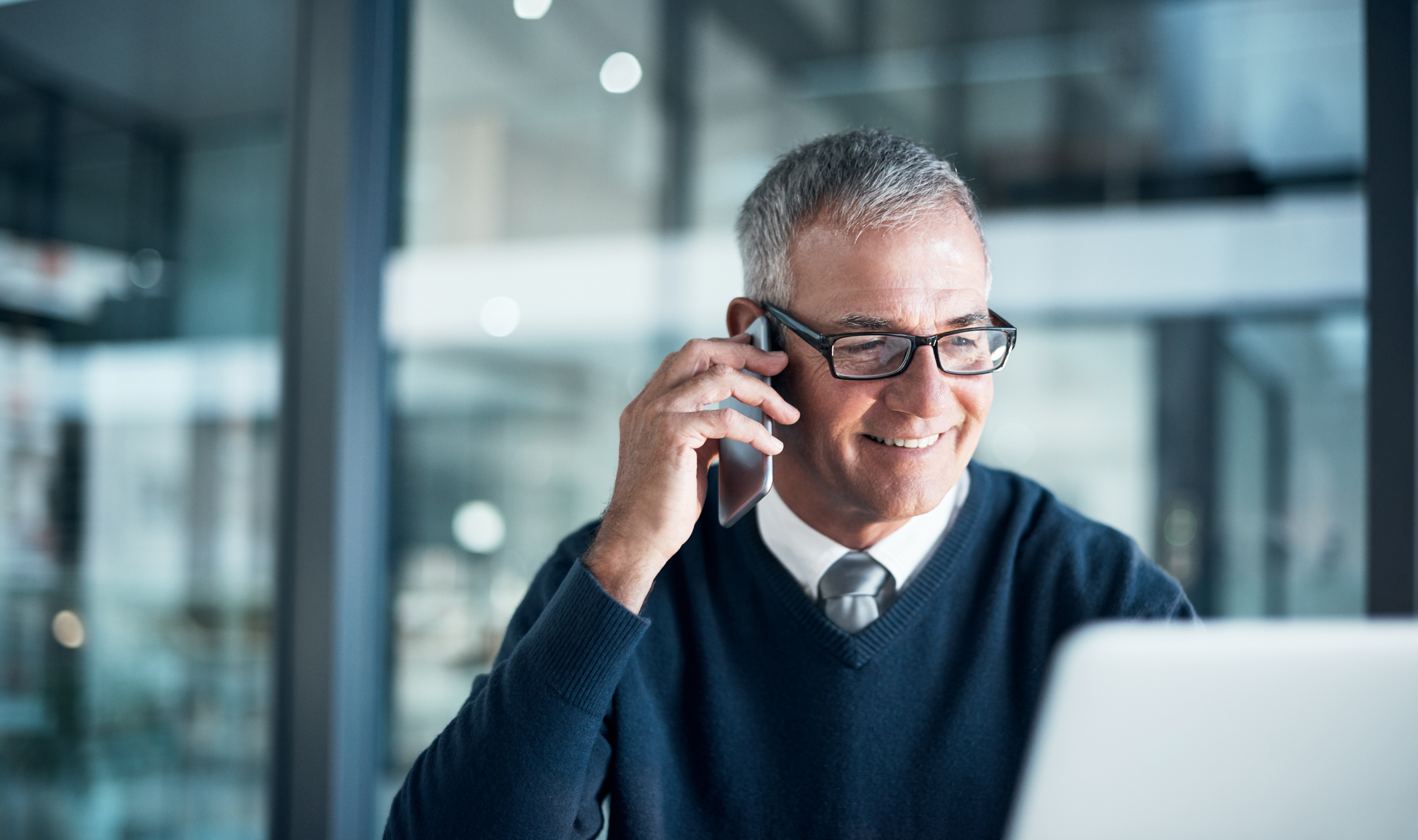 Shot of a mature businessman using a cell phone and laptop while working late in an office.  