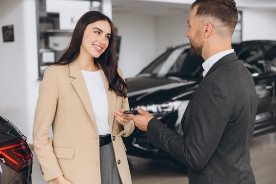 Smiling salesman or manager giving car keys to modern happy woman new car owner in car dealership.  