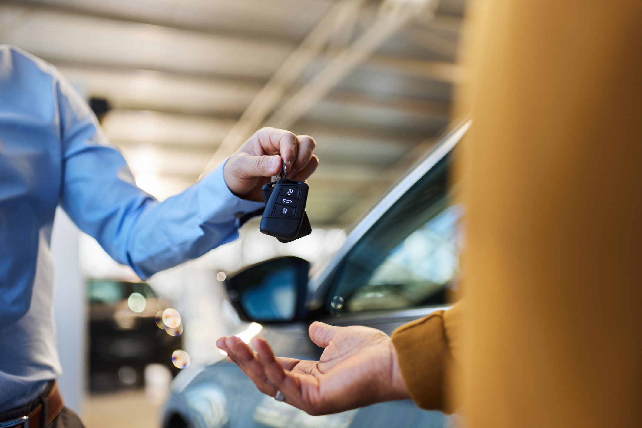 Close up of unrecognisable salesman giving car keys to his black customer in a showroom.