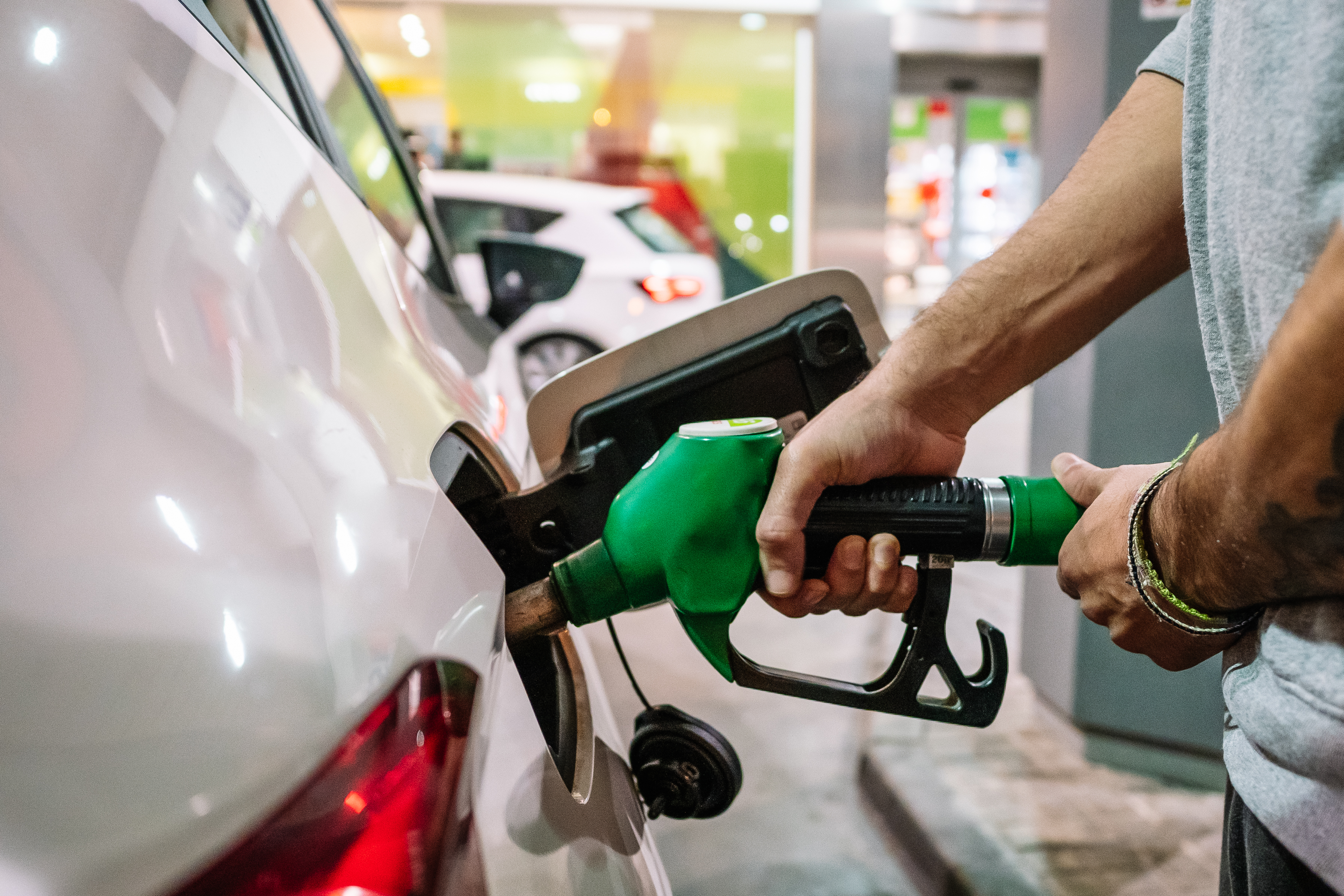 Unrecognisable male putting fuel dispenser in tank while refuelling vehicle on self-service gas station.  