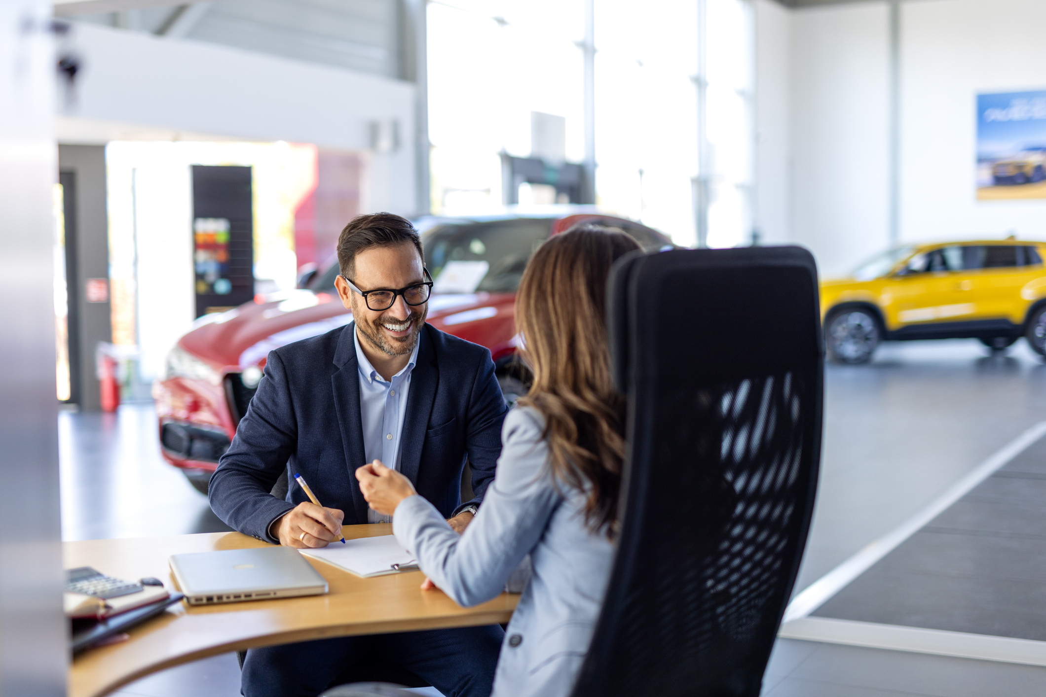 Smiling happy female manager car salesman in car dealership signing contract at table with male buyer in suit.  
