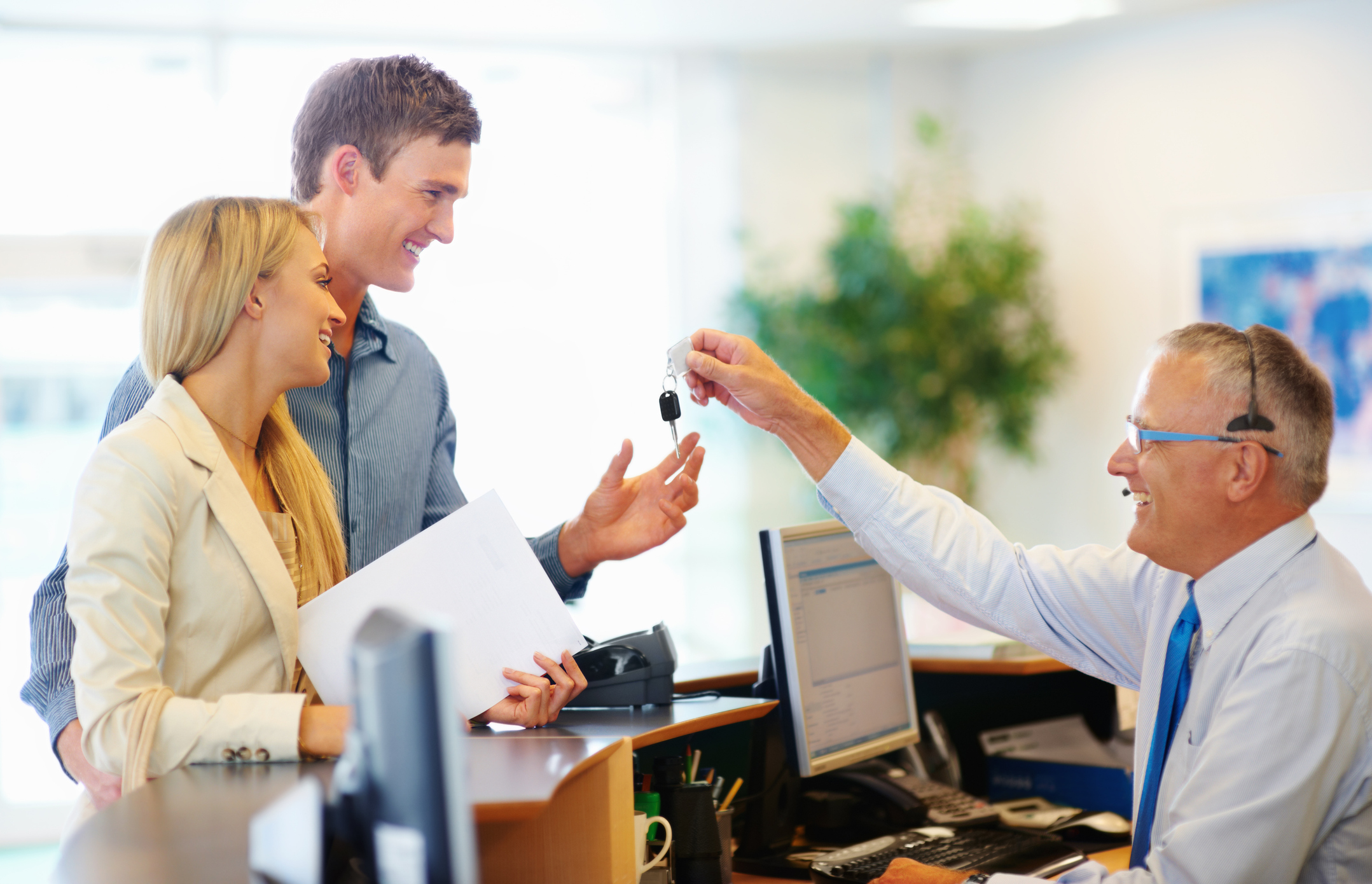 Senior employee handing a smiling couple the key to their car rental 