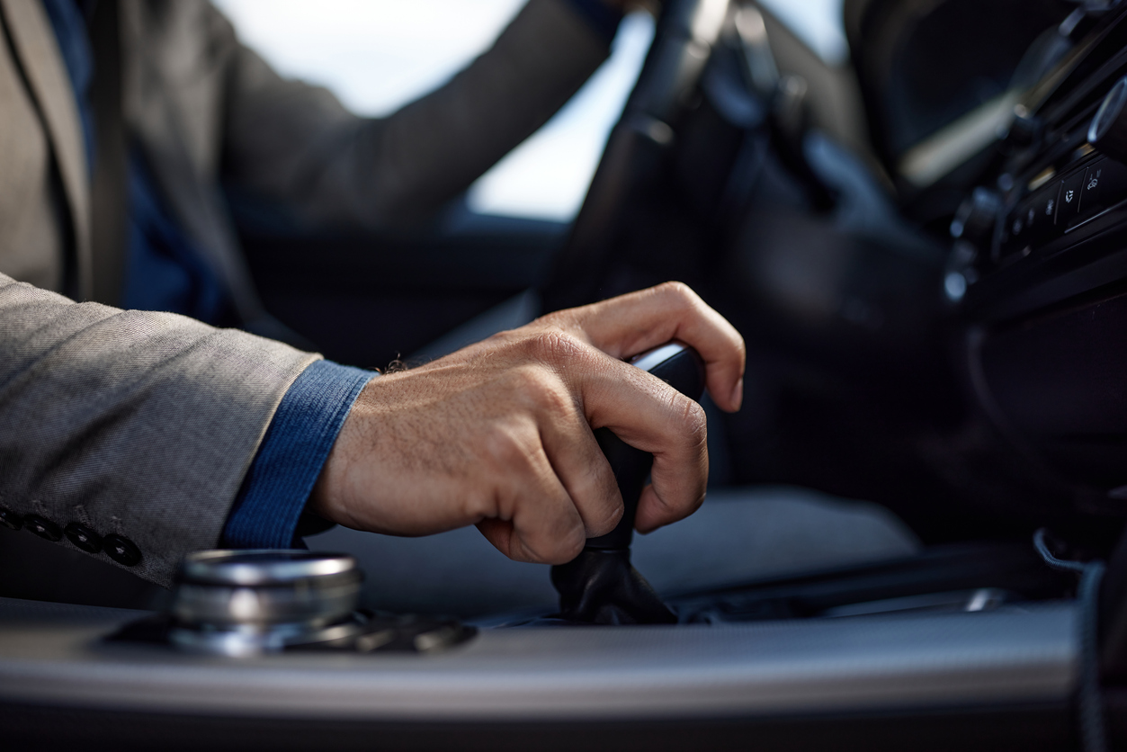 Close up of unrecognisable businessman holding his hand on automatic gearshift while driving a car. 