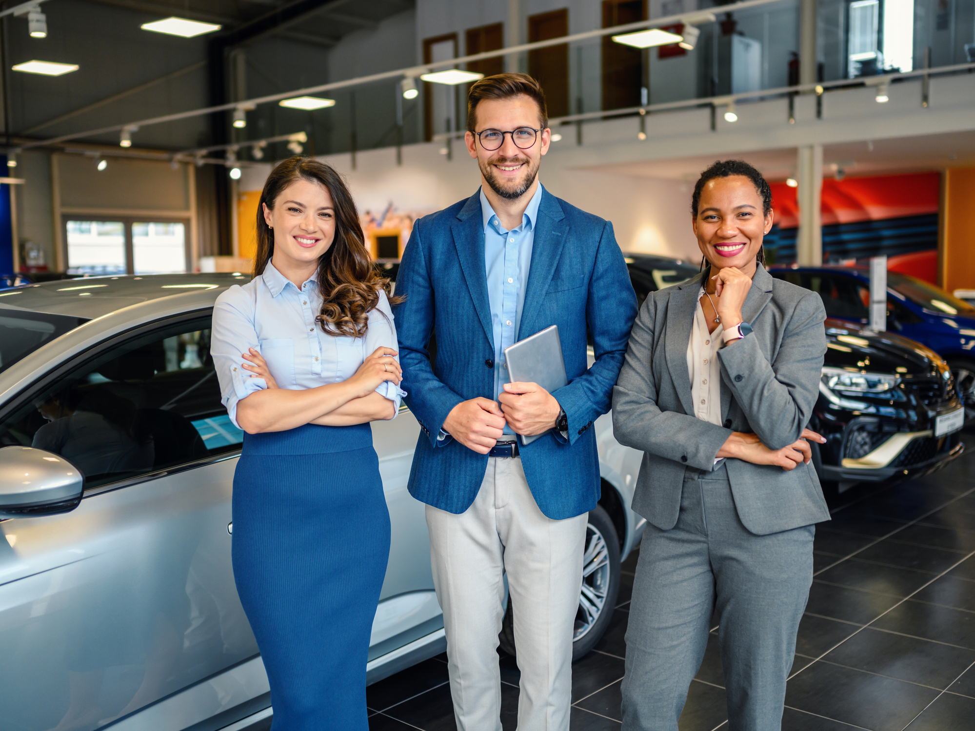 Portrait of the vehicle sales team with arms crossed inside a car showroom.  