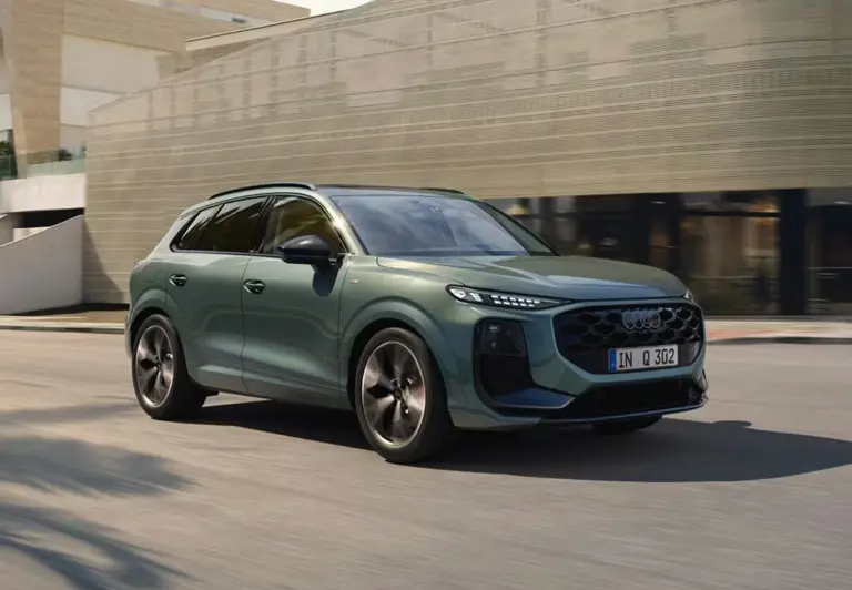The front and side of a green Audi Q3 driving past a modern city office building