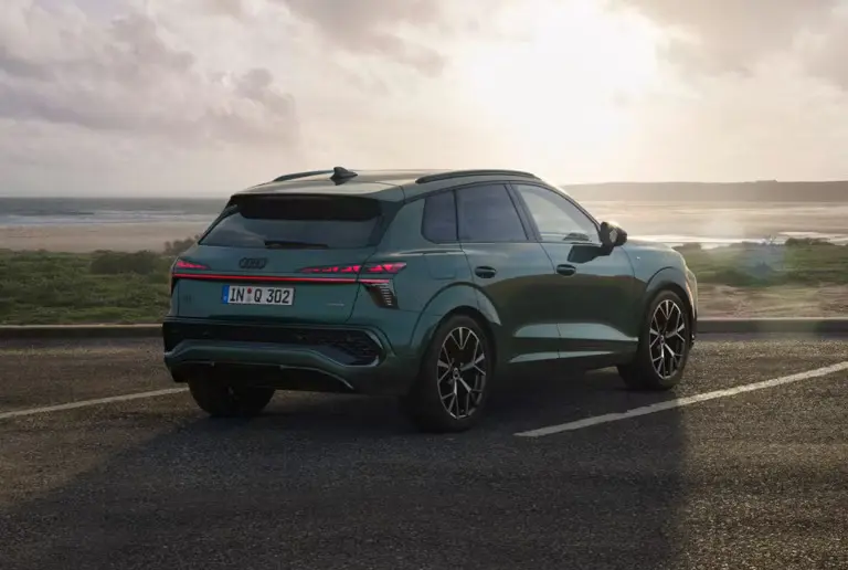 Rear view of a dark green Audi Q3 parked with ocean and cliff background at sunset