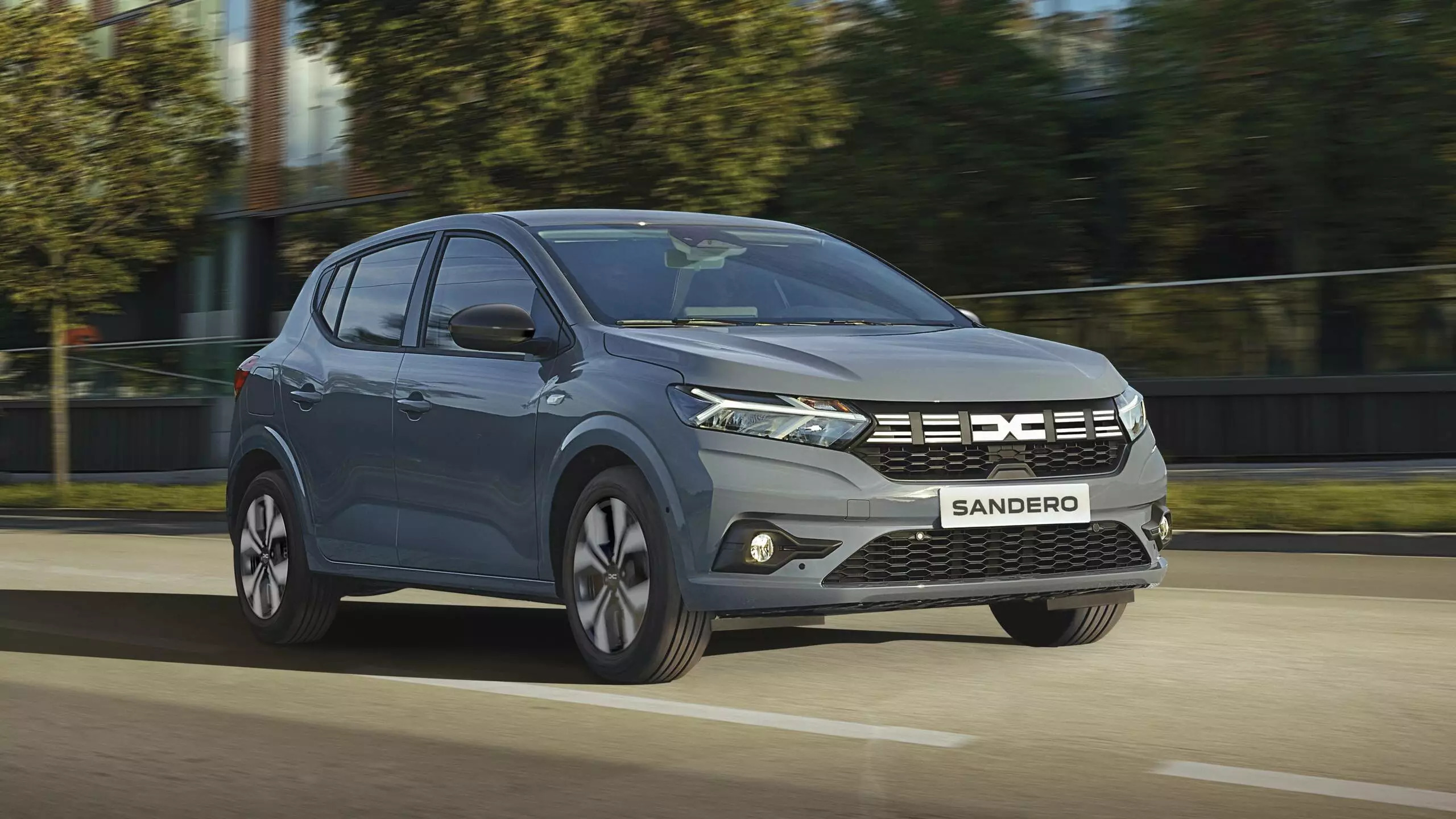 Grey Dacia Sandero car driving along the road with slightly blurred suburban background