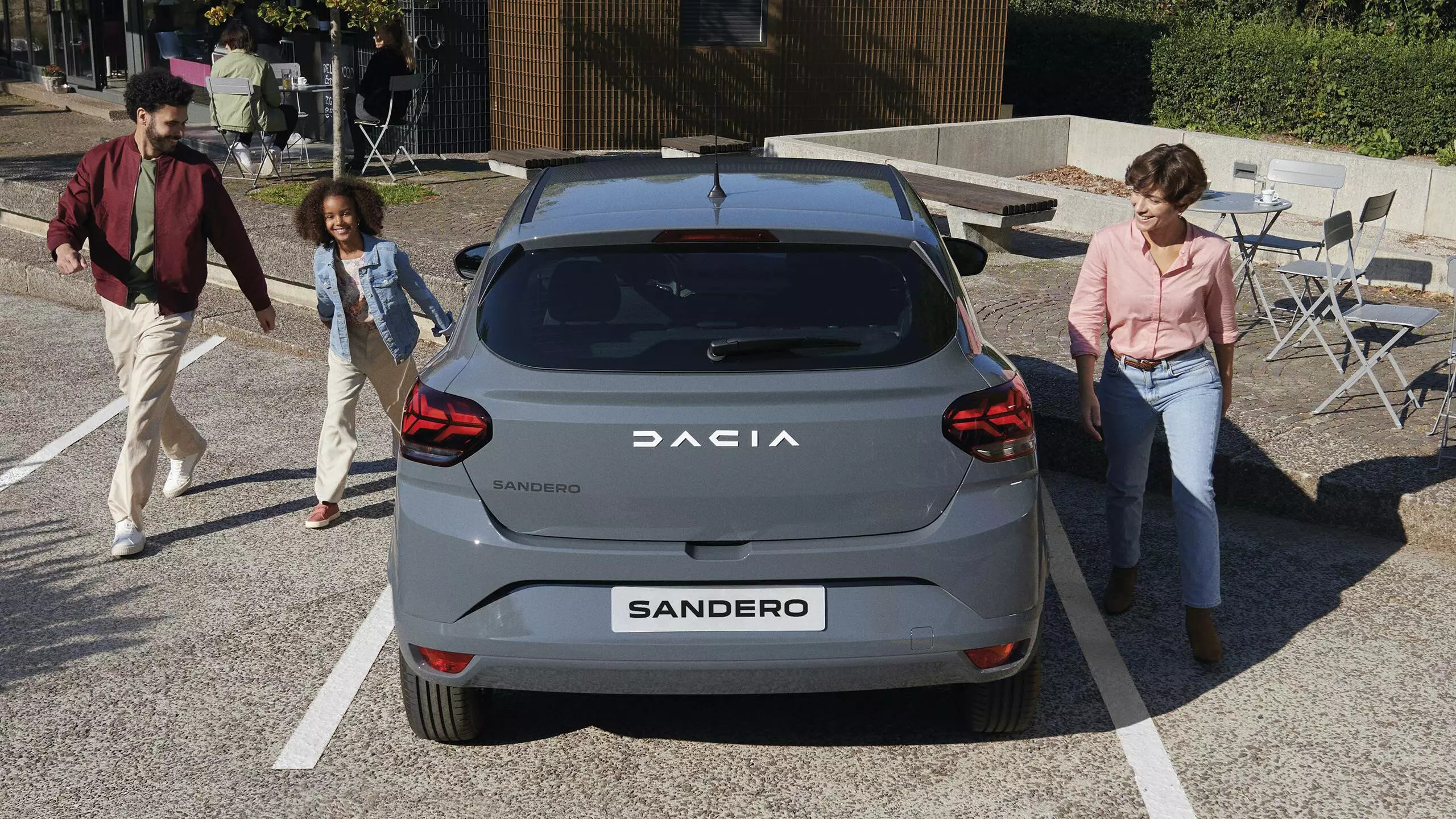A happy family ready for their day out after parking their grey Dacia Sandero outside a cafe
