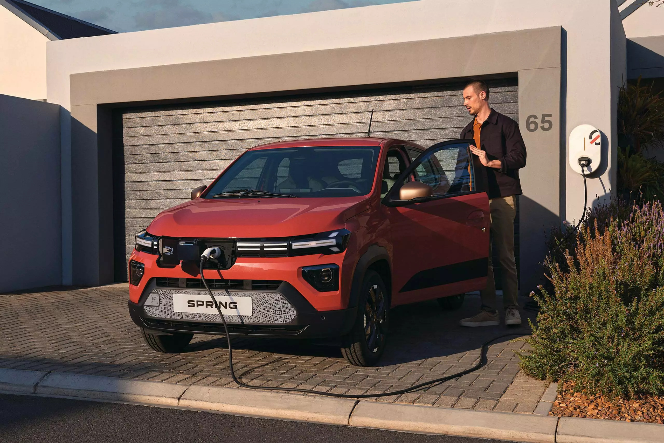 A man charging his orange electric vehicle (Dacia Spring) on his driveway