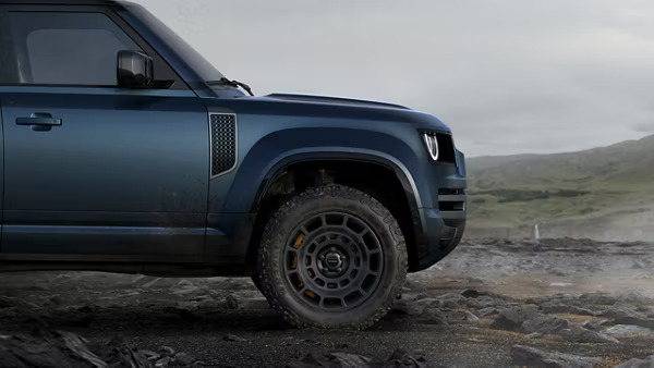 The side front end view of a navy-blue Land Rover Defender off-road with a countryside background