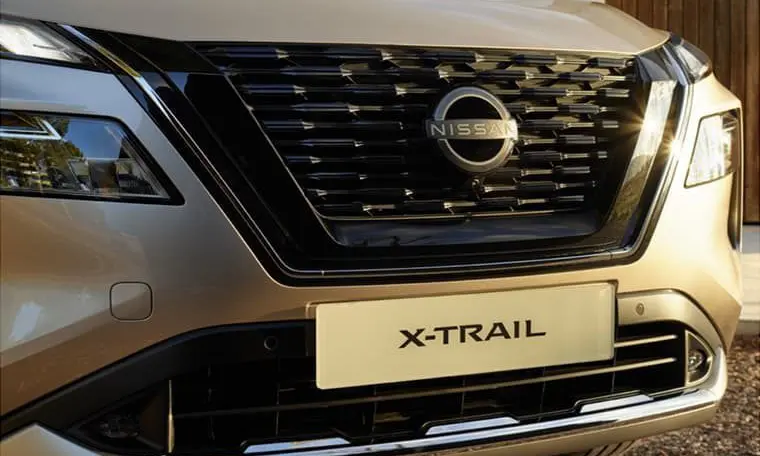close up shot of the front of a gold Nissan X-Trail parked on gravel