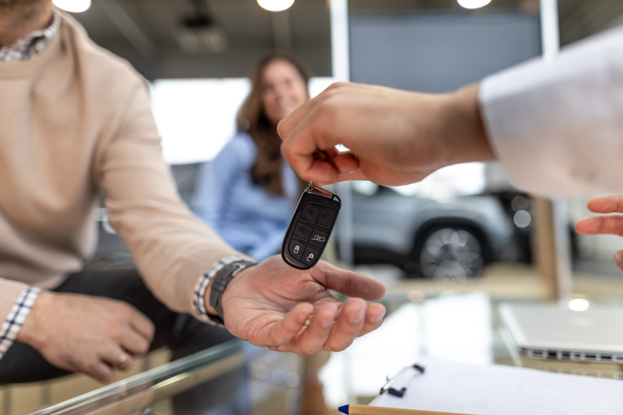 Car salesman handing over keys to a new car, solidifying the purchase agreement with a handshake, while a satisfied customer celebrates the achievement of car ownership in the dealership.