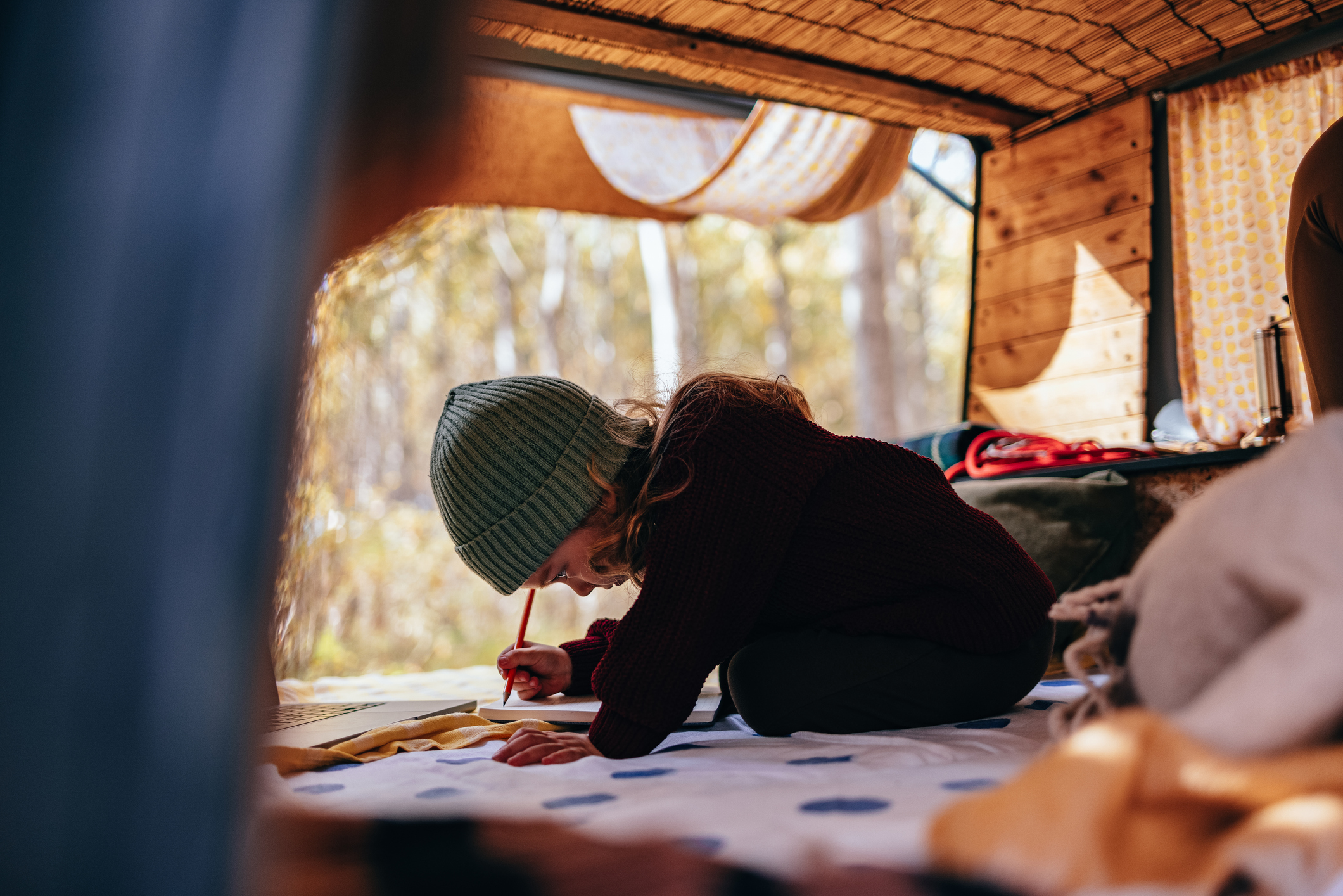 Smiling young girl sitting in a van and drawing in her notebook while camping in nature. 