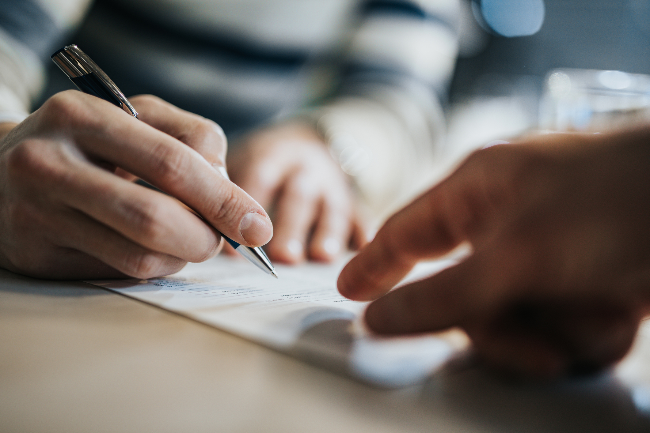 Close up of unrecognisable man signing a contract while financial advisor is aiming at the place he needs to sign. 